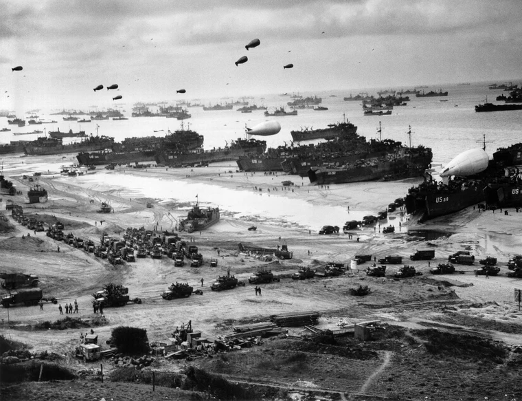 Allied supply ships and barrage balloons along Omaha Beach in the days after D-Day, showing the massive logistics operation