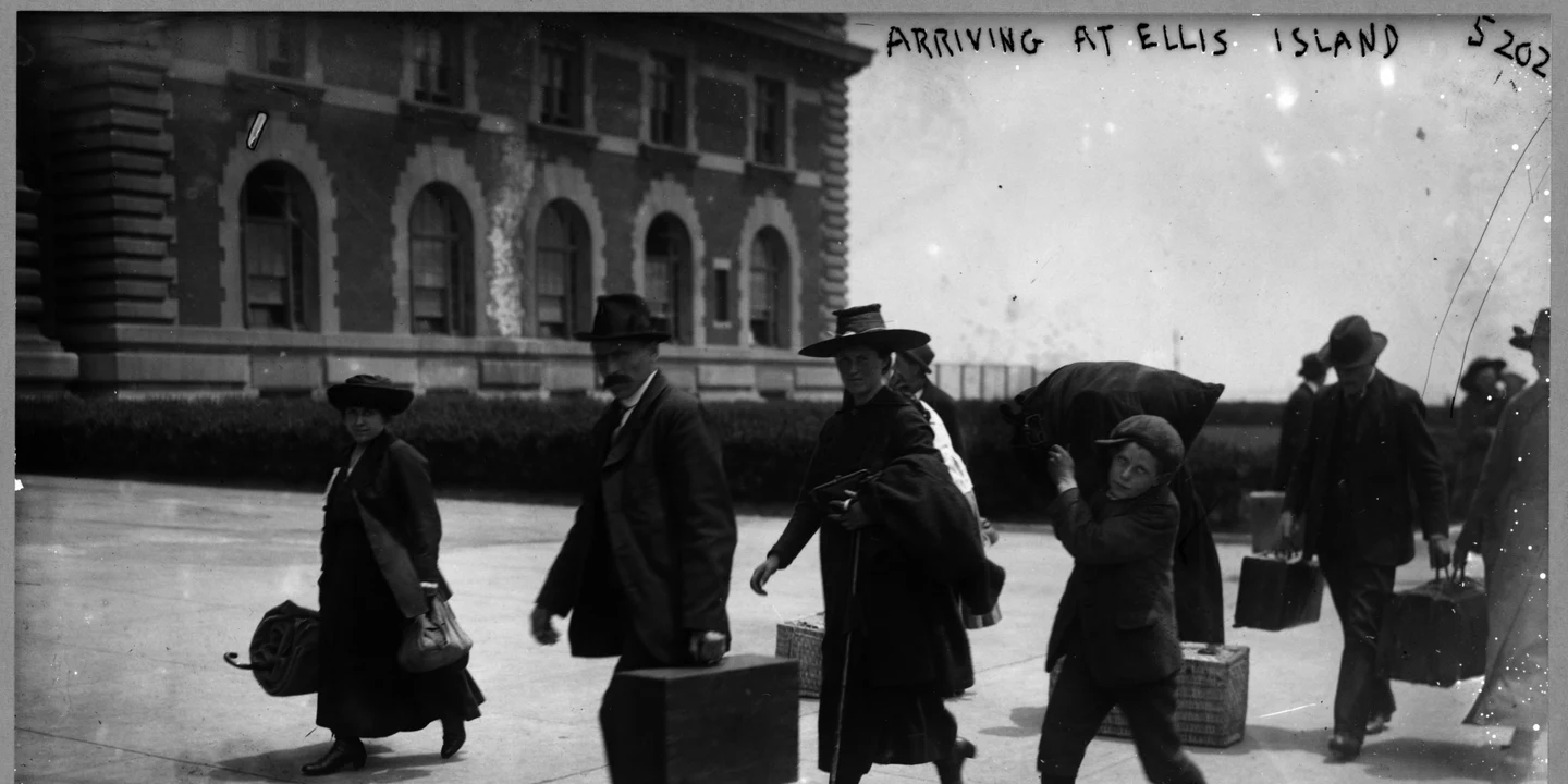 Immigrants arriving at Ellis Island carrying luggage and belongings — illustrating what is migration