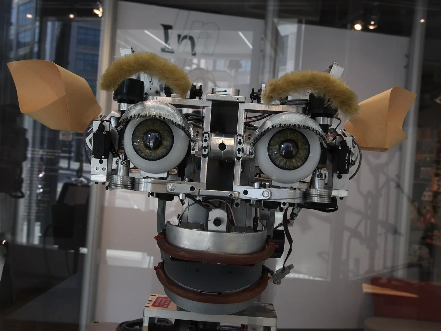 Kismet, a robot head with large eyes, eyebrows, ears and movable lips, on display behind glass