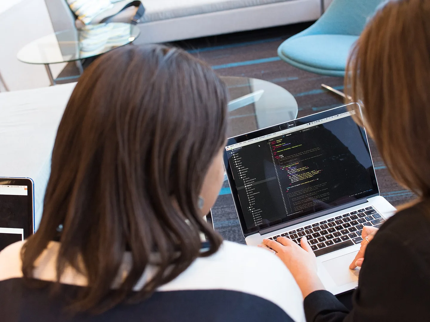 Two women at a laptop working through code together, seen over their shoulders