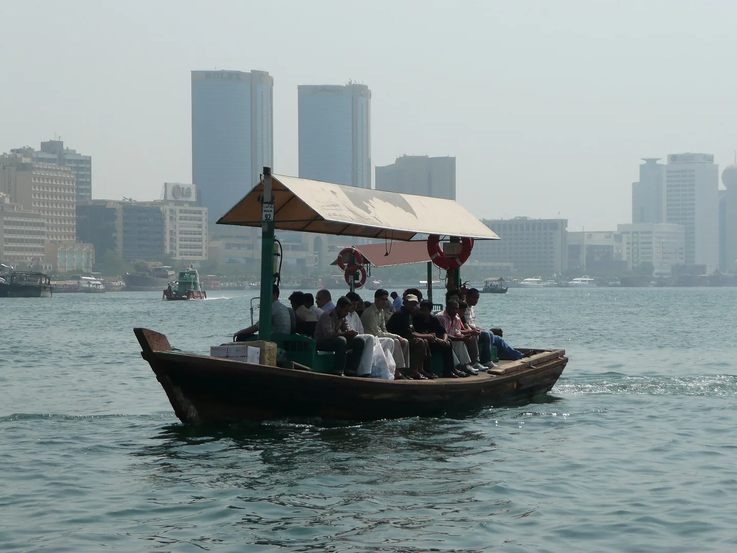 An abra water taxi carrying passengers across Dubai Creek, with the city's towers behind