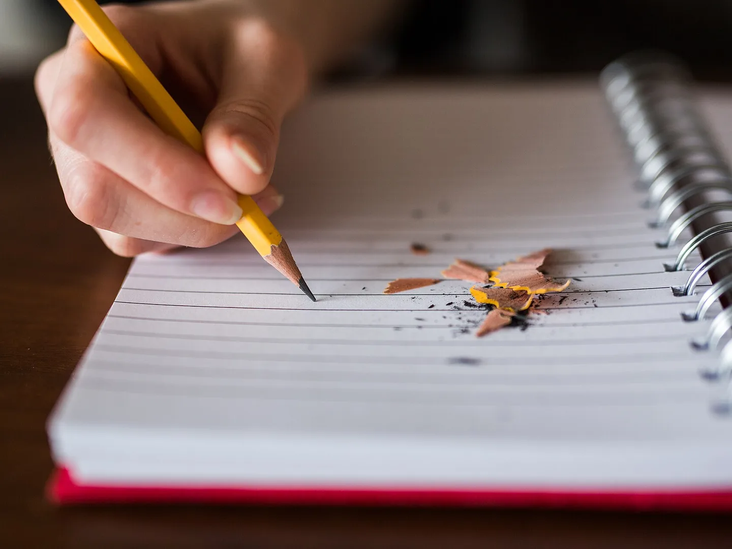 A hand taking notes with a pencil in a ring-bound notebook