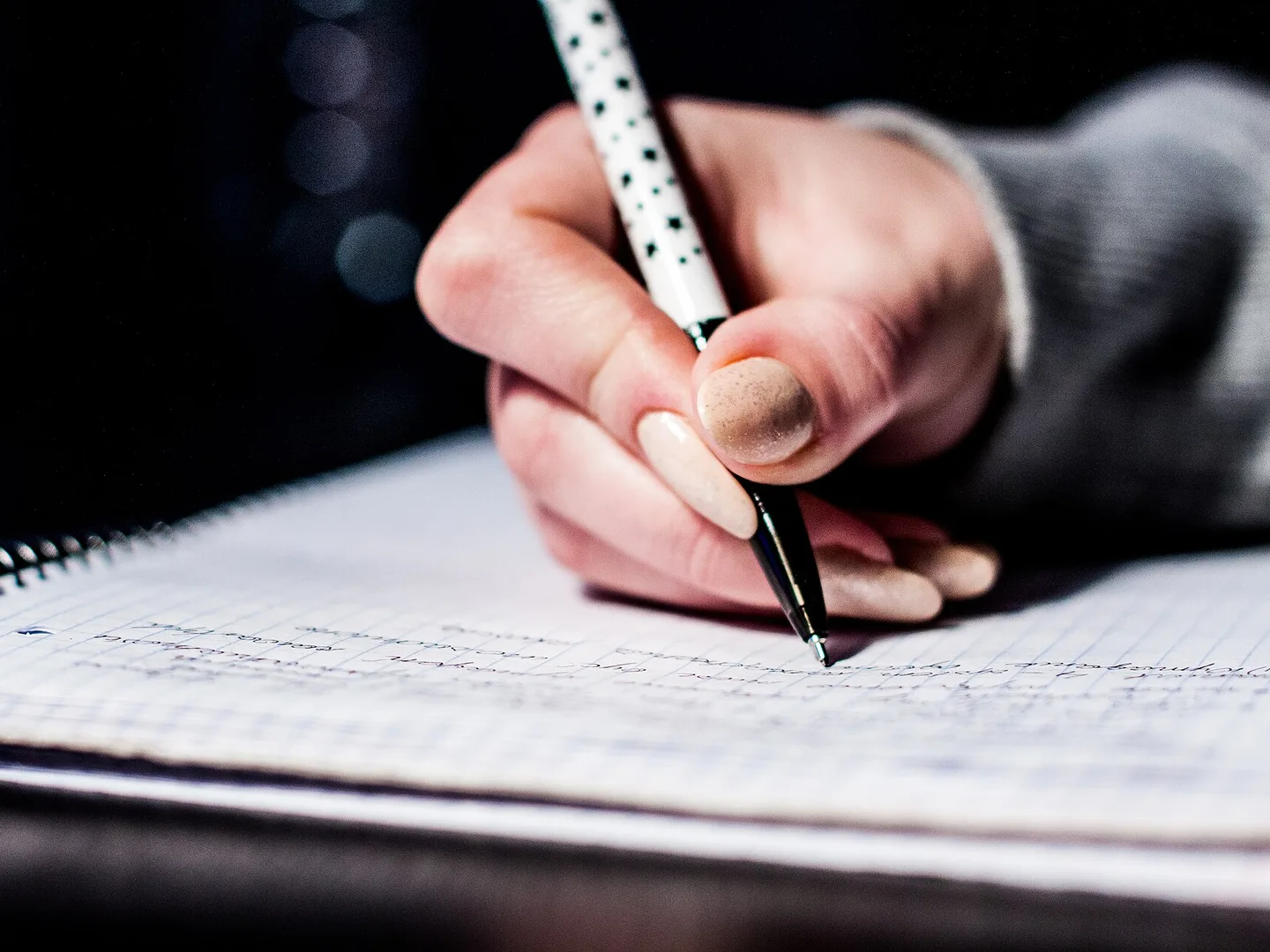 A hand writing notes with a pen in a squared notebook