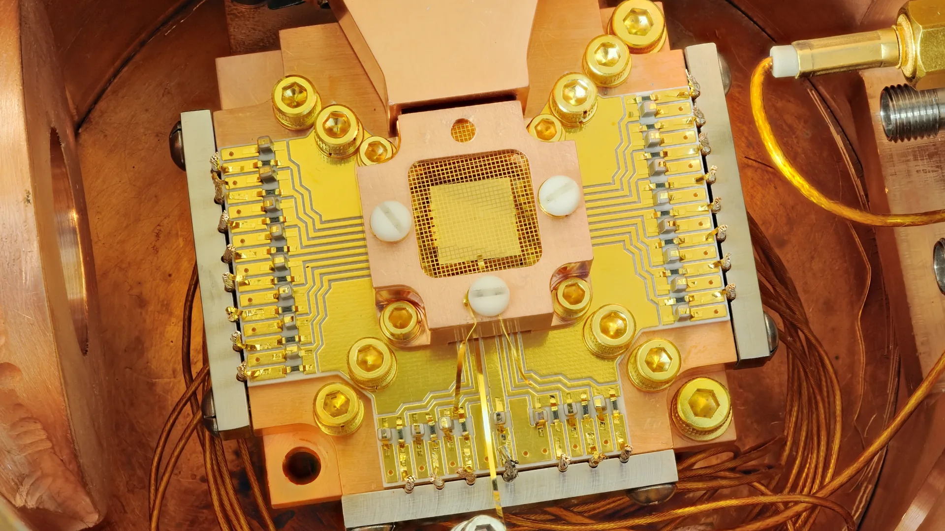 A gold-plated ion-trap chip with rows of electrodes, mounted in a copper vacuum housing and wired with fine copper leads