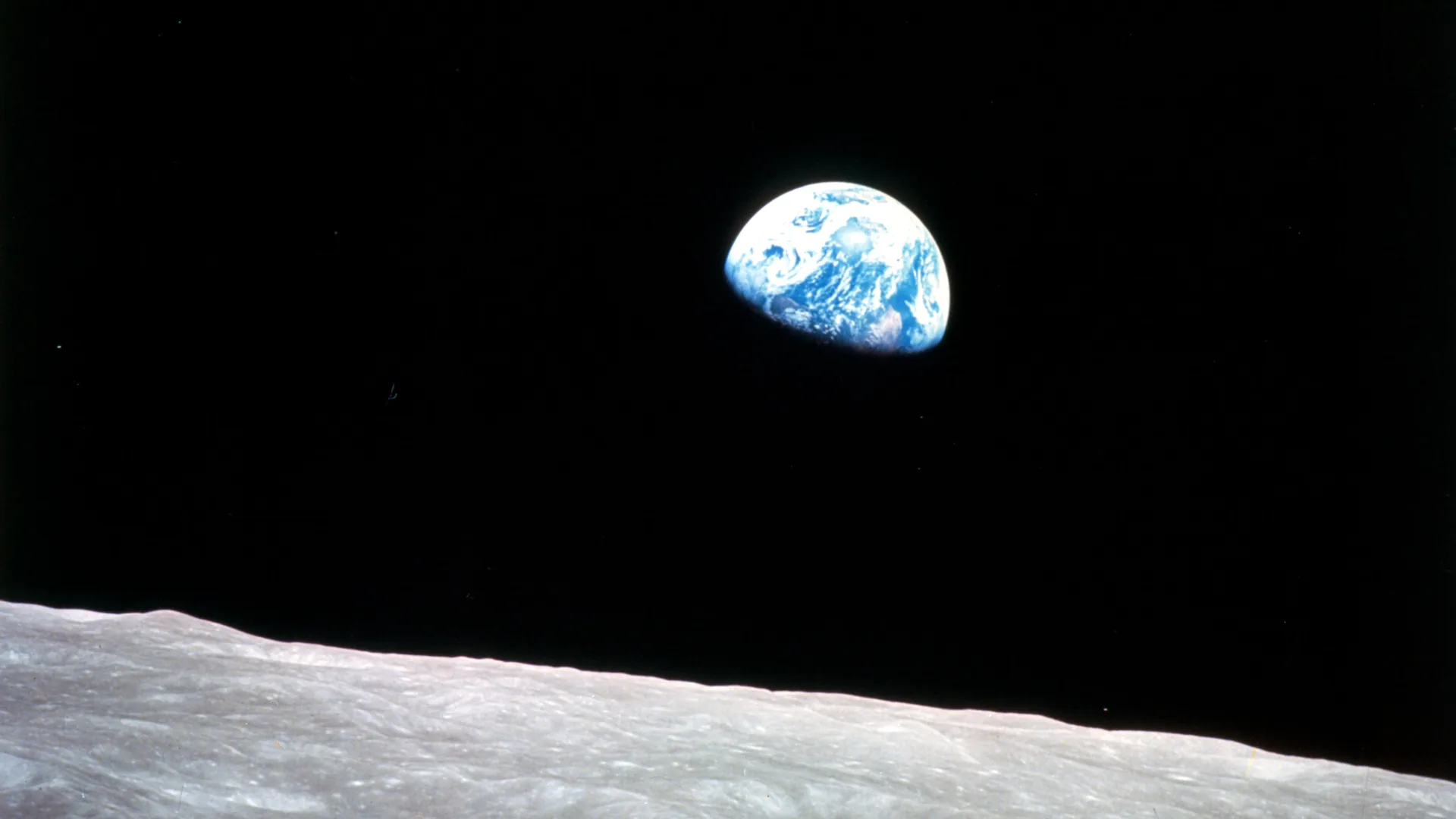 The Earth rising over the grey horizon of the Moon, half lit, against black space
